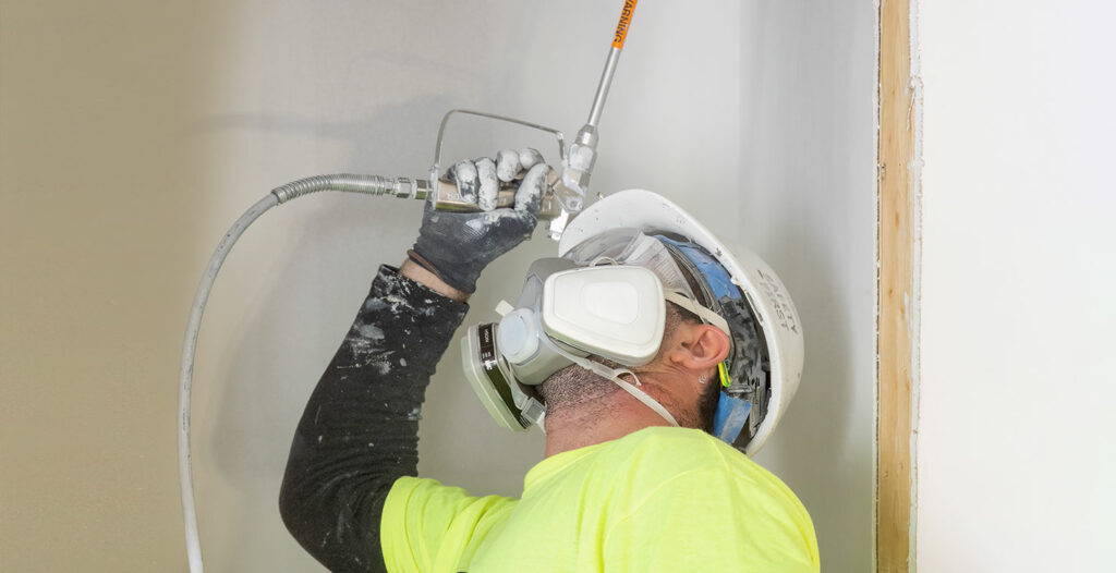 worker with mask painting a ceiling